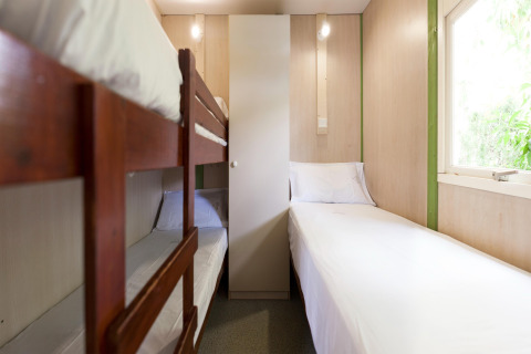 Habitación de lodge con litera de madera, cama individual, sábanas blancas y ventana luminosa.