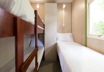 Habitación de lodge con litera de madera, cama individual, sábanas blancas y ventana luminosa.