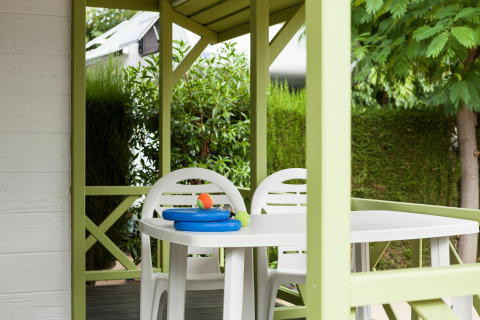 Terraza cubierta con sillas y mesa de plástico blanco, rodeada de plantas, en Camping Cambrils Playa.