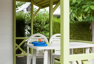 Terraza cubierta con sillas y mesa de plástico blanco, rodeada de plantas, en Camping Cambrils Playa.