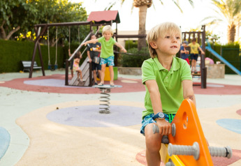 Niños juegan en un parque infantil colorido dentro de un alojamiento glamping en un día soleado.
