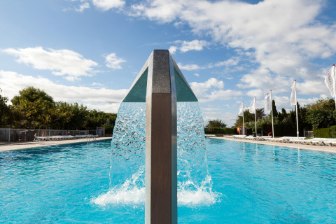 Udendørs swimmingpool med moderne vandfaldsfunktion under en klar himmel på et glamping-sted.