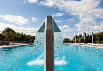 Piscina exterior con una moderna cascada de agua en un alojamiento glamping bajo un cielo parcialmente nublado.
