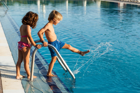 Dos niños en la piscina de un lodge; un niño salpica el agua mientras una niña lo observa cerca.