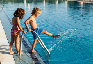 Dos niños en la piscina de un lodge; un niño salpica el agua mientras una niña lo observa cerca.
