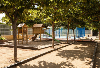 Parque infantil con estructura de madera y tobogán en Camping Cambrils Playa 1 BUNGALOW OASIS, España, rodeado de árboles.