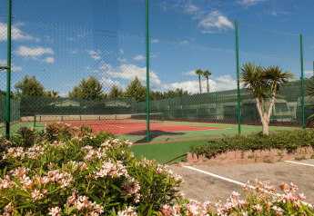 Pista de tenis al aire libre en alojamiento glamping, rodeada de flores, plantas y una valla verde.