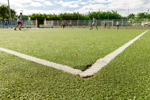 Niños juegan fútbol en un campo de césped artificial en un alojamiento glamping al aire libre.