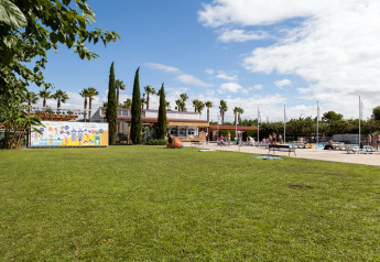 Zona de césped en Camping Cambrils Playa 2 BUNGALOW PREMIUM con piscina, tumbonas y palmeras en España.