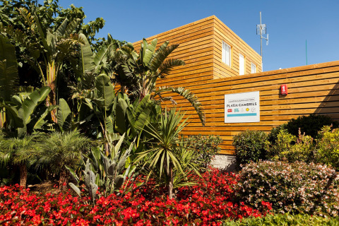 Ingang van Camping & Bungalow Park Platja Cambrils in Spanje met houten wanden, tropische planten en bloemen.