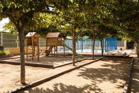 Buitenspeeltuin met houten speelhuisjes en glijbaan naast sportveld bij een glamping-accommodatie.