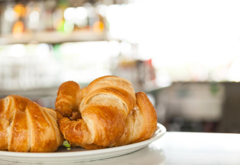 Croissants frescos servidos en un plato en una posada, con un fondo brillante y desenfocado.