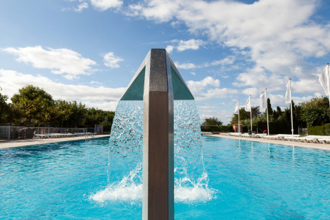 Piscina exterior con moderno chorro de agua bajo el cielo azul en Camping Cambrils Playa 1 BUNGALOW OASIS, España.