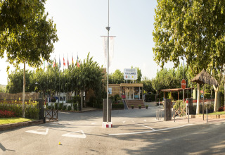 Ingang van een lodge met vlaggen, bomen en receptie, zonnige dag en ontspannen sfeer buiten.