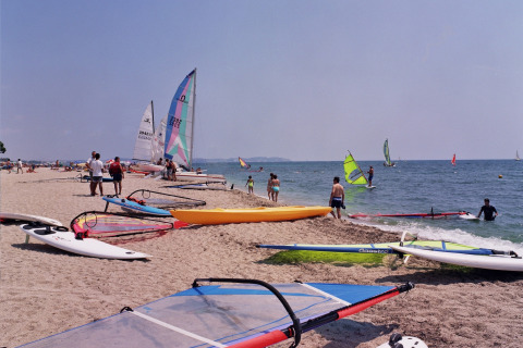 Strand bij Camping Cambrils Playa 2 BUNGALOW PREMIUM in Spanje, met surfplanken, boten en bezoekers.