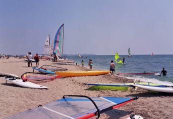Playa en Camping Cambrils Playa 2 BUNGALOW PREMIUM, España, con tablas y barcos de windsurf y visitantes.