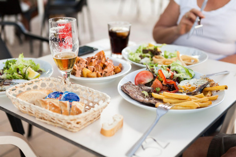 Tafel in een lodge met diverse gerechten zoals vlees, friet, salade, brood en verschillende drankjes.