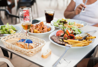 Tafel in een lodge met diverse gerechten zoals vlees, friet, salade, brood en verschillende drankjes.