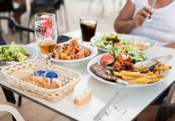 Mesa en una posada con varios platos como carne, papas fritas, ensalada, pan y diferentes bebidas.