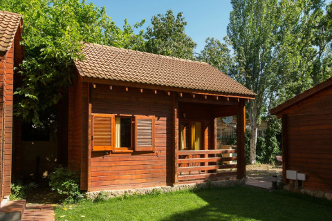 Træhytte med terrasse og åbne vinduer på La Llosa 1 Xaloc-lodgen, omgivet af grønne træer.