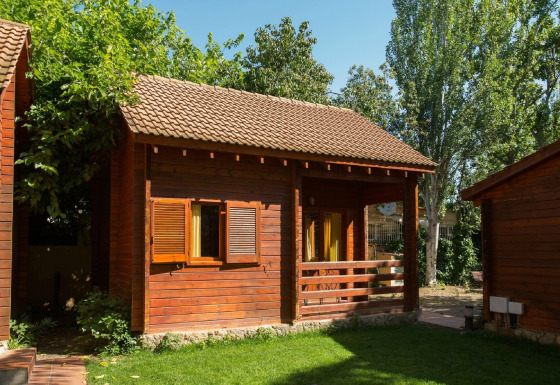 Træhytte med terrasse og åbne vinduer på La Llosa 1 Xaloc-lodgen, omgivet af grønne træer.