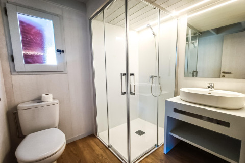 Moderne badeværelse på La Llosa 1 Xaloc i Spanien med bruseniche, toilet og håndvask på hvid bordplade.