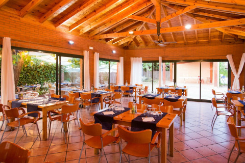Salle de restaurant lumineuse en glamping, mobilier en bois moderne et larges baies ouvertes sur la verdure.