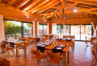 Salle de restaurant lumineuse en glamping, mobilier en bois moderne et larges baies ouvertes sur la verdure.