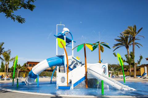 Aire de jeux aquatique colorée avec toboggans et palmiers dans un lodge sous un ciel bleu clair.