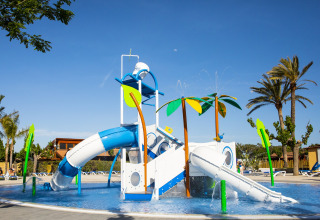 Aire de jeux aquatique colorée avec toboggans et palmiers dans un lodge sous un ciel bleu clair.
