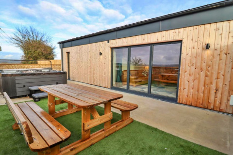 Buitenruimte aan Little Rissington - Barn Four met houten picknickbank, bubbelbad en grote schuiframen.