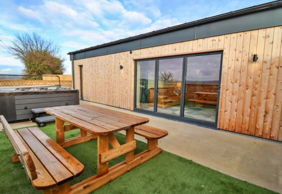 Buitenruimte aan Little Rissington - Barn Four met houten picknickbank, bubbelbad en grote schuiframen.