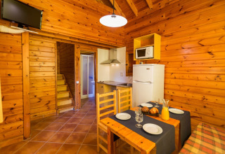 Træhytteinteriør i La Llosa 1 Xaloc, Spanien, med spisebord, køkken og pejs.