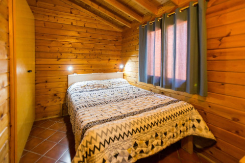 Chambre avec murs en bois, lit double et fenêtre à rideaux, photographiée à la lodge La Llosa Ponent en Espagne.