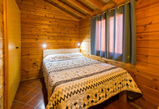Chambre avec murs en bois, lit double et fenêtre à rideaux, photographiée à la lodge La Llosa Ponent en Espagne.