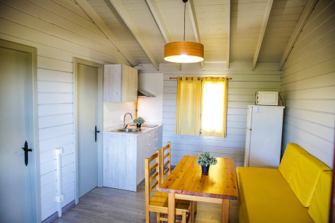 Intérieur douillet d’un lodge à La Llosa Ponent, Espagne, avec cuisine, table à manger et canapé jaune.