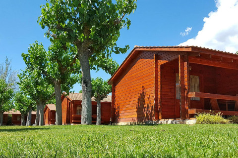 Charmants chalets en bois à La Llosa Ponent, bordés de pelouse et d’arbres sous un ciel bleu clair.