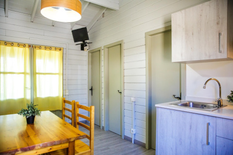 Intérieur du lodge La Llosa Ponent en Espagne avec table à manger, kitchenette, portes et téléviseur.