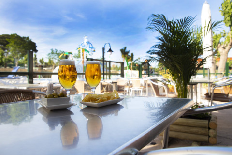 Deux verres de bière et des snacks sur une table extérieure dans un glamping avec vue sur piscine et verdure.