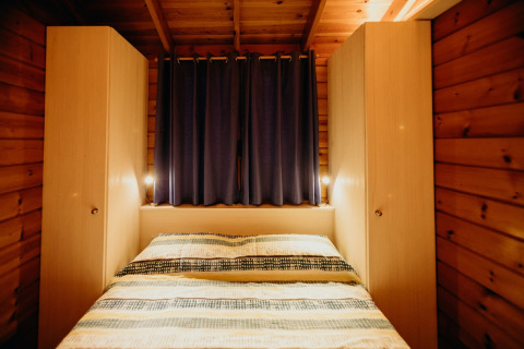 Camera da letto in legno della cabina La Llosa 3 LLEBEIG in Spagna con letto, armadi e tende blu.