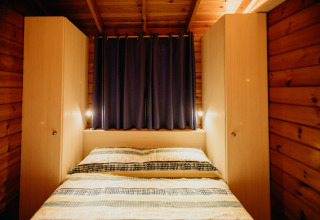 Camera da letto in legno della cabina La Llosa 3 LLEBEIG in Spagna con letto, armadi e tende blu.