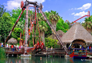 Manège bateau coloré avec visiteurs et lodges de glamping dans un cadre tropical verdoyant et aquatique.