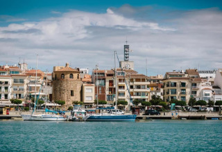 Vue sur un port pittoresque avec voiliers, tour en pierre et hébergement glamping moderne en bord de mer.