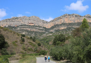 Deux personnes marchent près du lodge La Llosa Ponent en Espagne, entourées de falaises rocheuses et verdure.