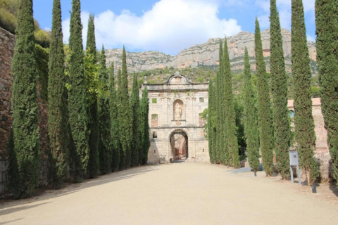 Entrée de la loge La Llosa Ponent en Espagne, bordée de cyprès et dominée par un paysage montagneux.
