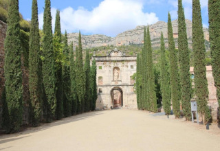 Entrée de la loge La Llosa Ponent en Espagne, bordée de cyprès et dominée par un paysage montagneux.