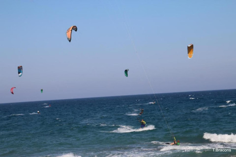 Scène de kitesurf colorée sur la mer près d’un glamping, cerfs-volants flottant sous un ciel bleu.