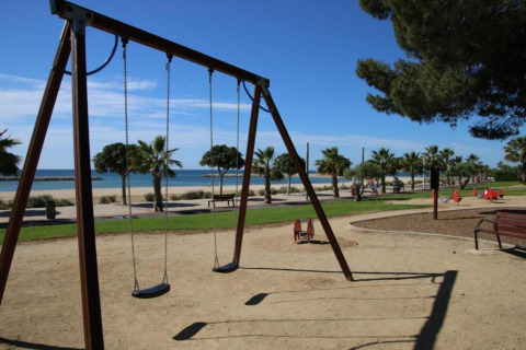 Aire de jeux avec balançoires et palmiers près de la plage à la lodge La Llosa Ponent en Espagne, journée ensoleillée