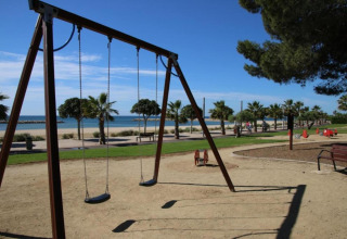 Aire de jeux avec balançoires et palmiers près de la plage à la lodge La Llosa Ponent en Espagne, journée ensoleillée