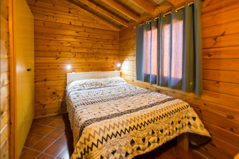 Camera della lodge La Llosa Mestral-BUNGALOWS-G in Spagna con pareti in legno, letto e finestre con tende.